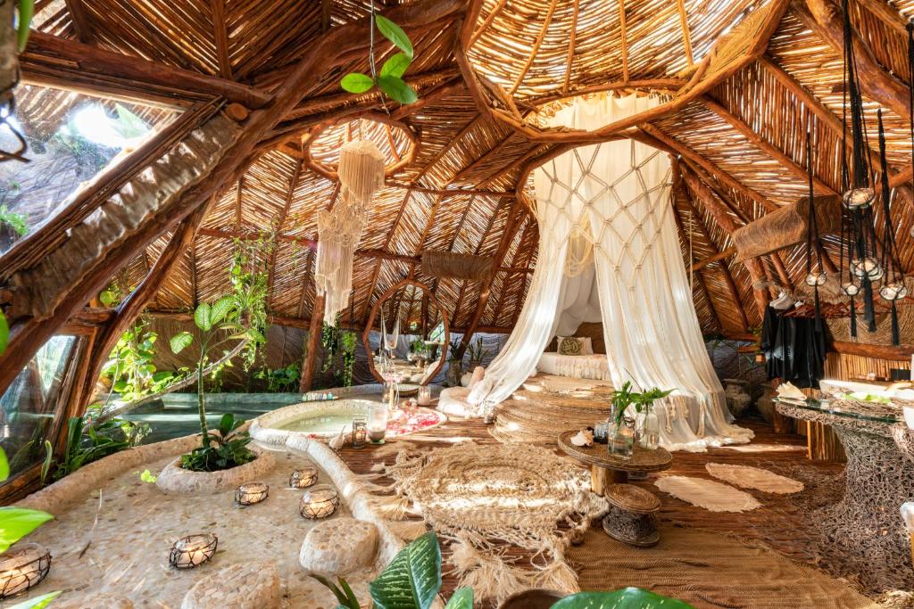 Quarto do Azulik (chamado Villa Aqua), de 130 m², com decoração rústica usando materiais da natureza como madeira, galhos de árvore, tapetes artesanais e flores. Há uma cama, hidro e espelho redondo grande.