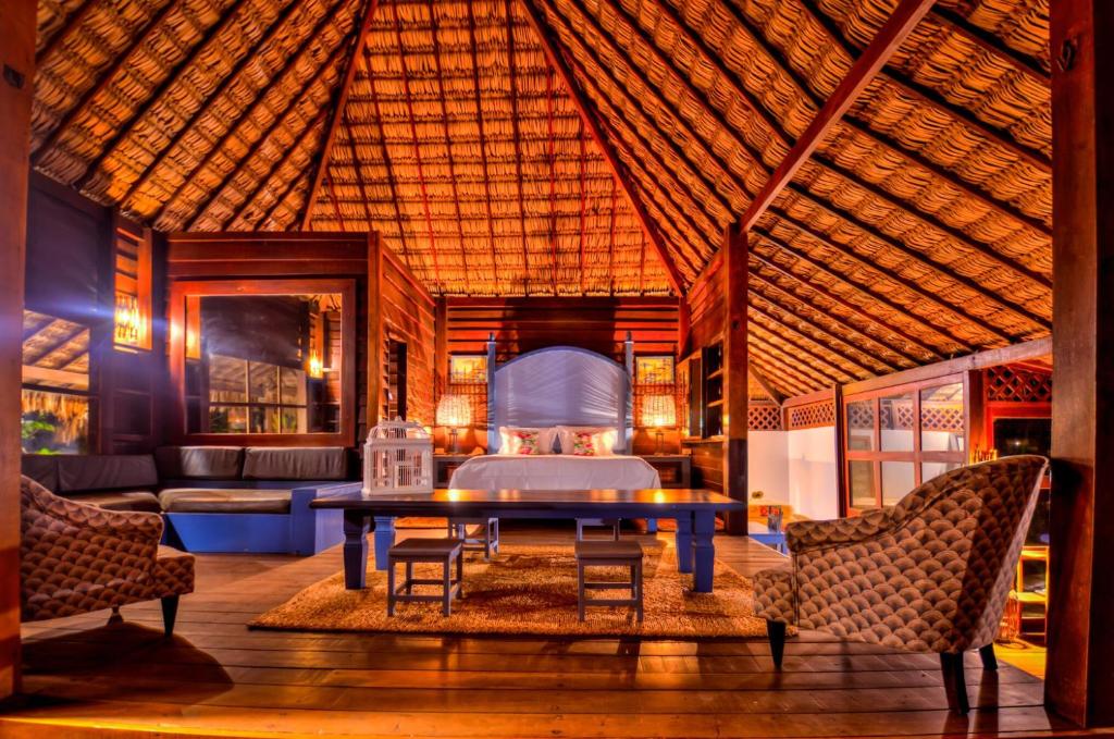 Quarto duplo deluxe da Baía das Caraúbas, de 110 m², com paredes e chão de madeira, duas poltronas, uma mesa retangular, sofá e cama de casal.