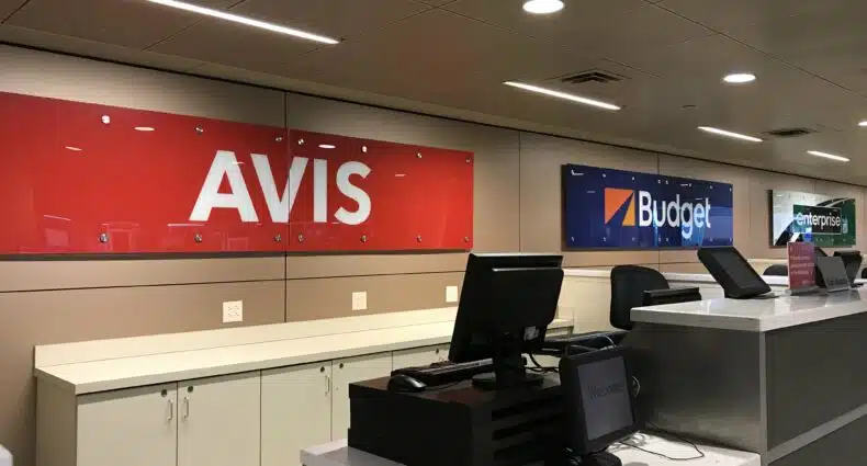 Balcão da Avis Rent a Car, com placa indicativa da companhia, uma mesa com computador e armários atrás, no Aeroporto de Dallas Love Field
