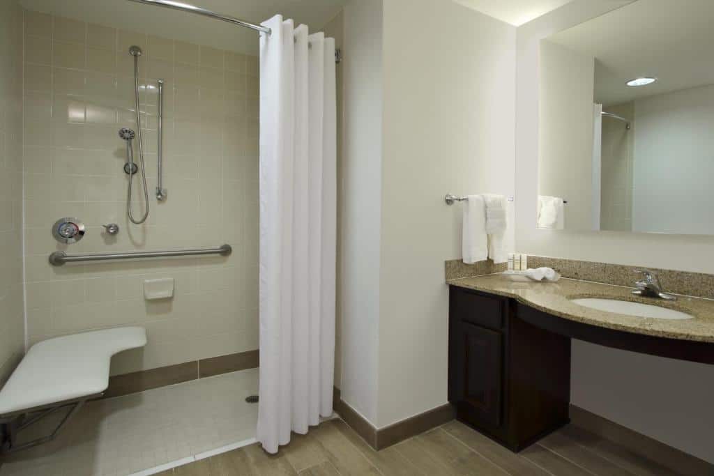Banheiro com acessibilidade do Homewood Suites by Hilton Miami – Airport West com pia baixa, chuveiro com barras de segurança. Representa Hotéis com cozinha em Miami.