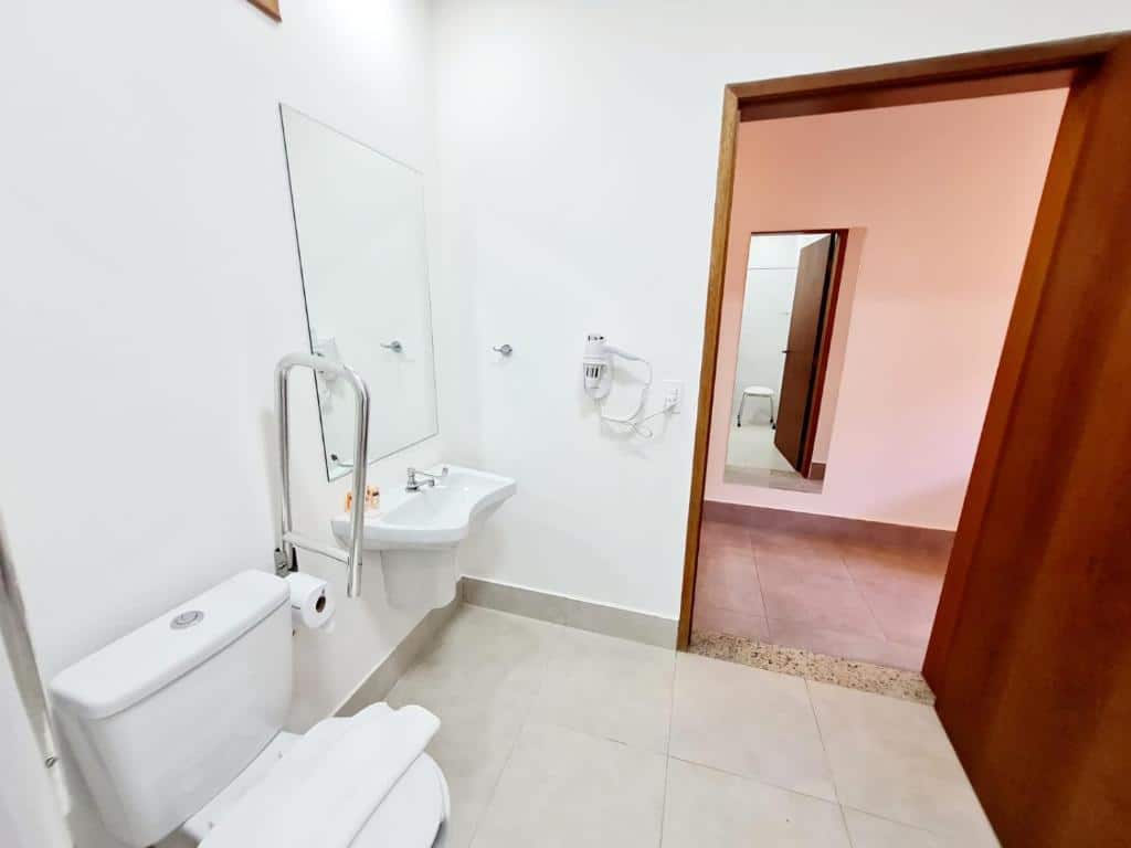 Banheiro com acessibilidade da Pousada Vila Ipuan com vaso sanitário, com barra de segurança ao lado, pia baixa e porta ampla. Representa pousadas na praia de Santiago.