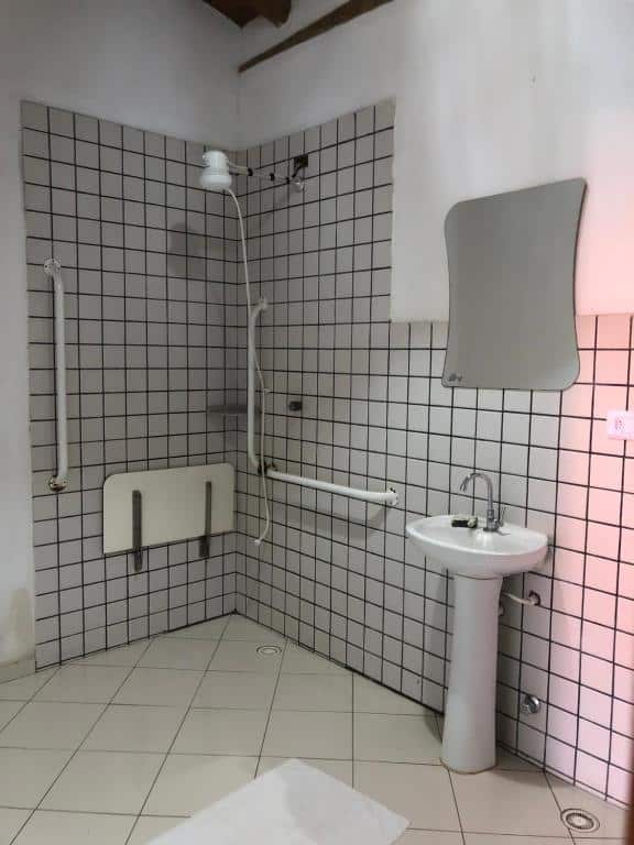 Banheiro com acessibilidade da  Pousada Vila Cambury com barras de segurança perto do chuveiro e pia baixa.