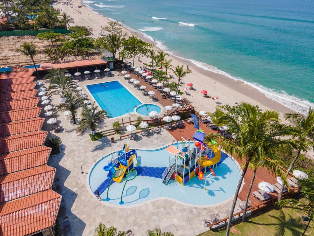 Piscina do Beach Hotel Maresias virada em direção da areia da praia, com algumas palmeiras ao redor e mesinhas com guarda-sóis no deck ao redor da piscina