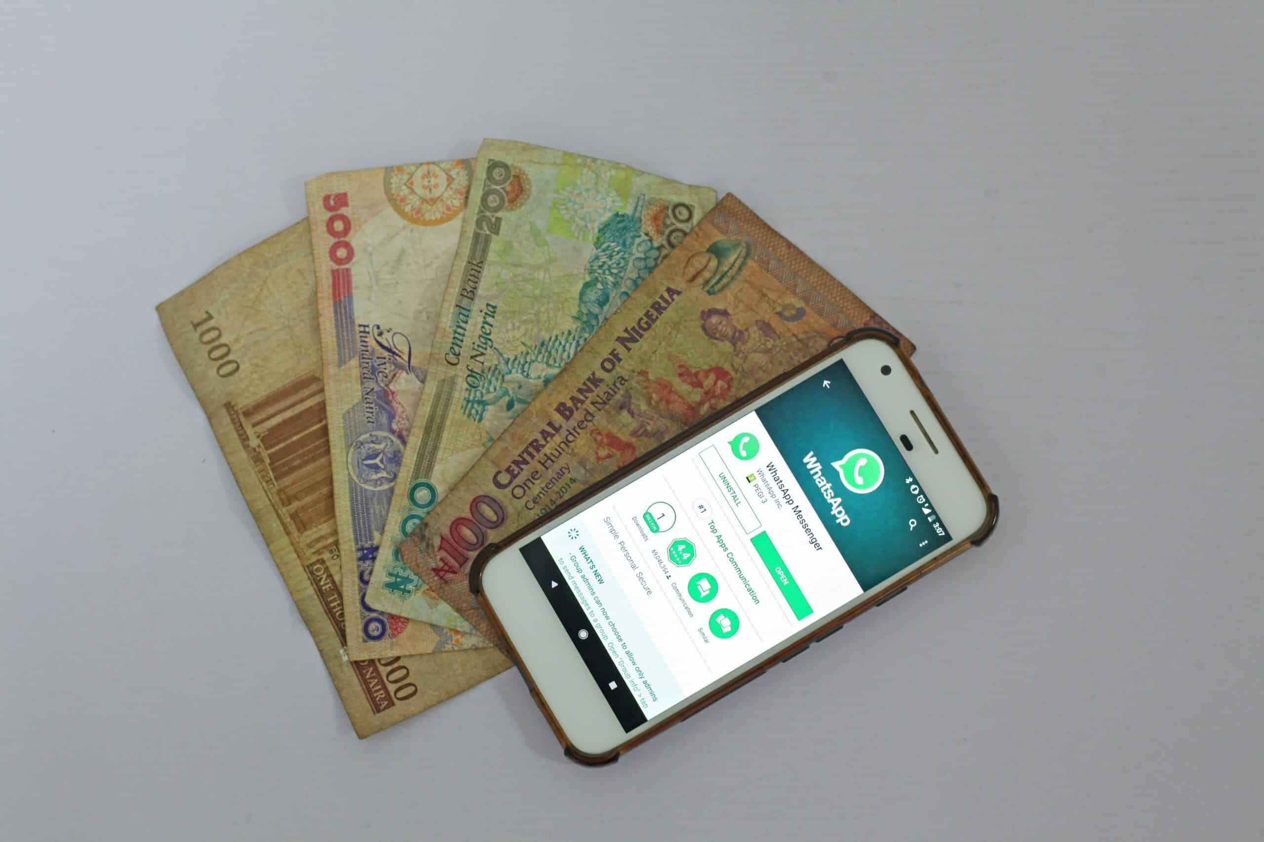 mesa branca vista de cima com um celular android aberto no aplicativo Whatsapp, em cima de quatro nota nigerianas de diferentes valores