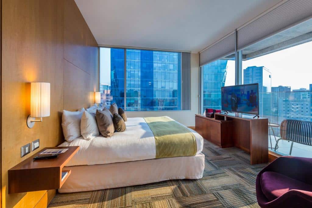 Quarto do Best Western Premier Marina Las Condes com cama de casal do lado esquerdo uma cômoda de madeira com TV.