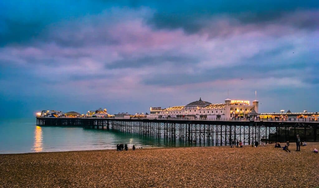 Pier de Brighton e faixa de areia com pessoas em frente ao mar durante ao anoitecer.