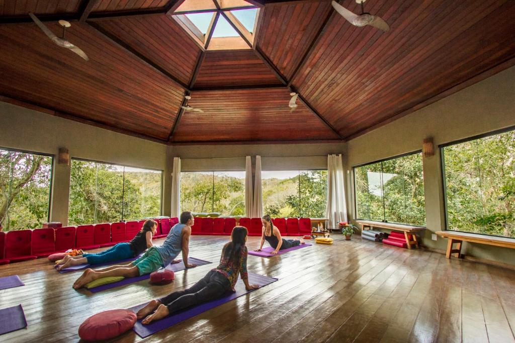 Um local inteiro de madeira e cercado pelo verde no Buzios Espiritualidade Hotel com pessoas praticando yoga no local com orientação de uma professora