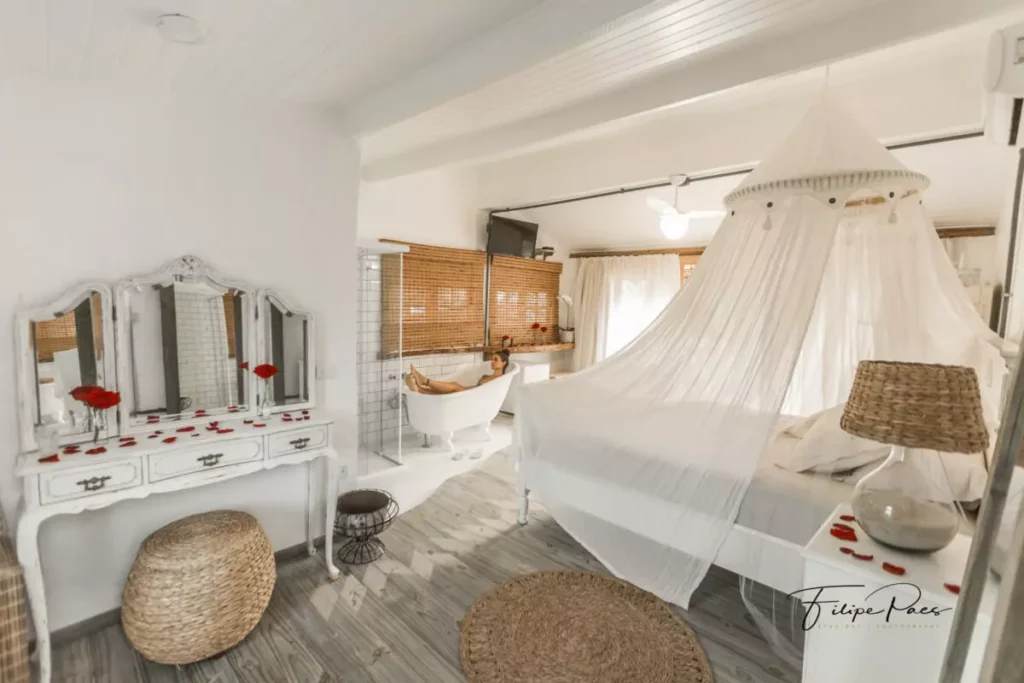 Quarto da Cabana Charmosa Pé na Areia em Maresias – Luai Cabanas com uma cama estilo bangalô, uma banheira, uma penteadeira e muitos itens rústicos