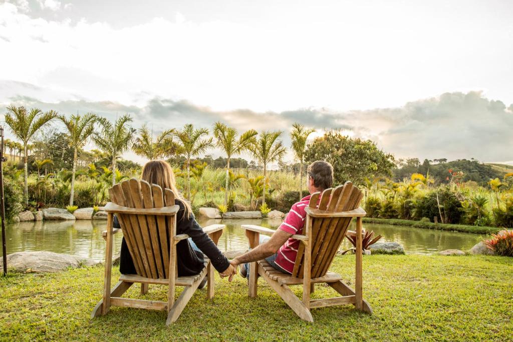 Duas cadeiras de madeira com um casal sentada olhando um lago cercado por montanhas nas Cabanas Portal da Serra