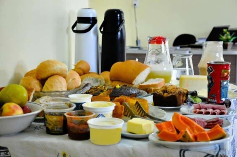 mesa do café da manhã com vários pães, geleias, garrafas térmicas de café e jarras de suco na Pousada Aparados em Cambará do Sul