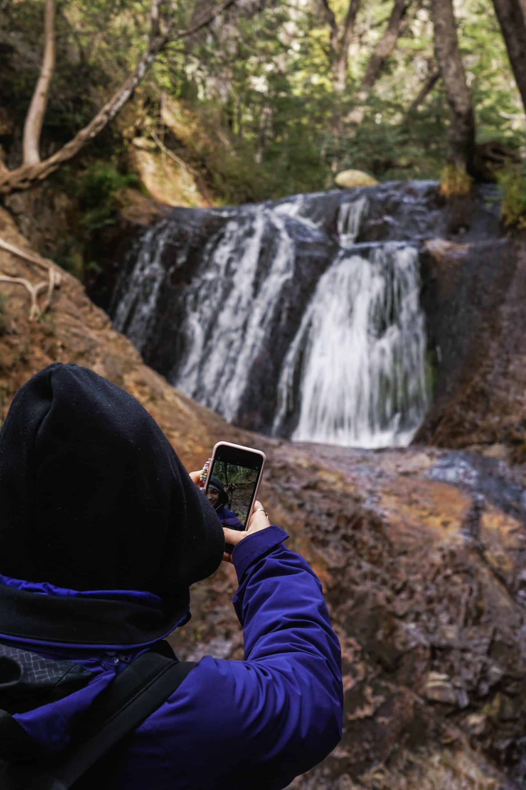 mulher tirando uma selfie em uma região de mata fechada com uma beça cachoeira a frente dela para representar o chip de celular em San Carlos de Bariloche