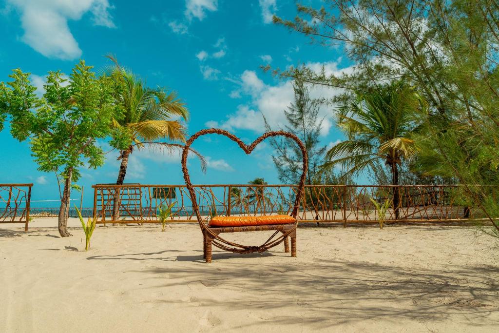 Área reservada à beira-mar do Camozen Resort & Spa, com um banco artesanal no formato de coração. Há árvores, a areia é branca e o mar está ao fundo