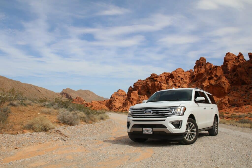 Carro grande e branco da Ford em estrada de cascalhos numa paisagem de deserto, no Valley of Fire Highway, nos Estados Unidos