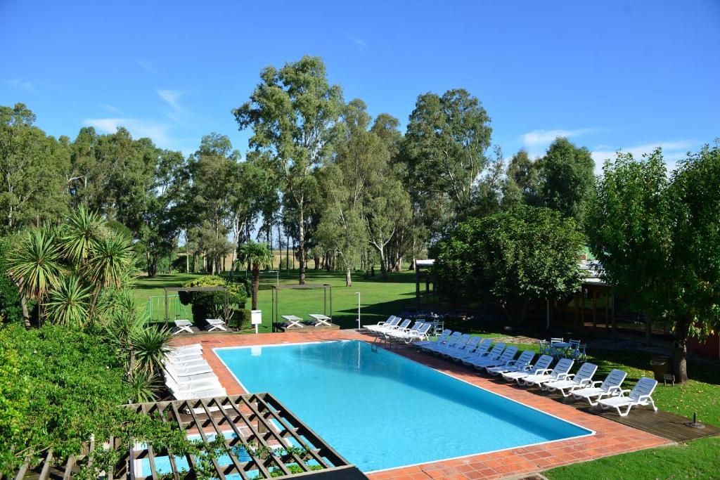 Piscina do Casa del Sol Hotel & Restaurante com um amplo jardim ao redor com árvores e algumas espreguiçadeiras brancas ao redor do deck da piscina, para representar hotéis em Colonia del Sacramento