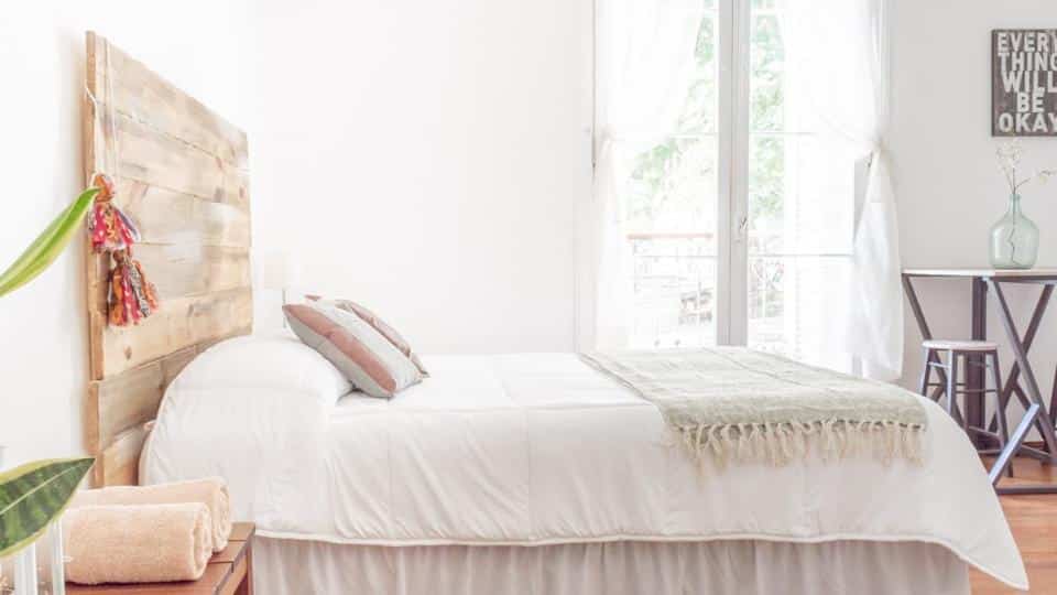 Quarto da Casa Francis - Apartamentos com uma sacada com cortinas, são de madeira, uma cama de casal, uma mesinha com dois banquinhos, tudo em madeira e estilo clean rústico