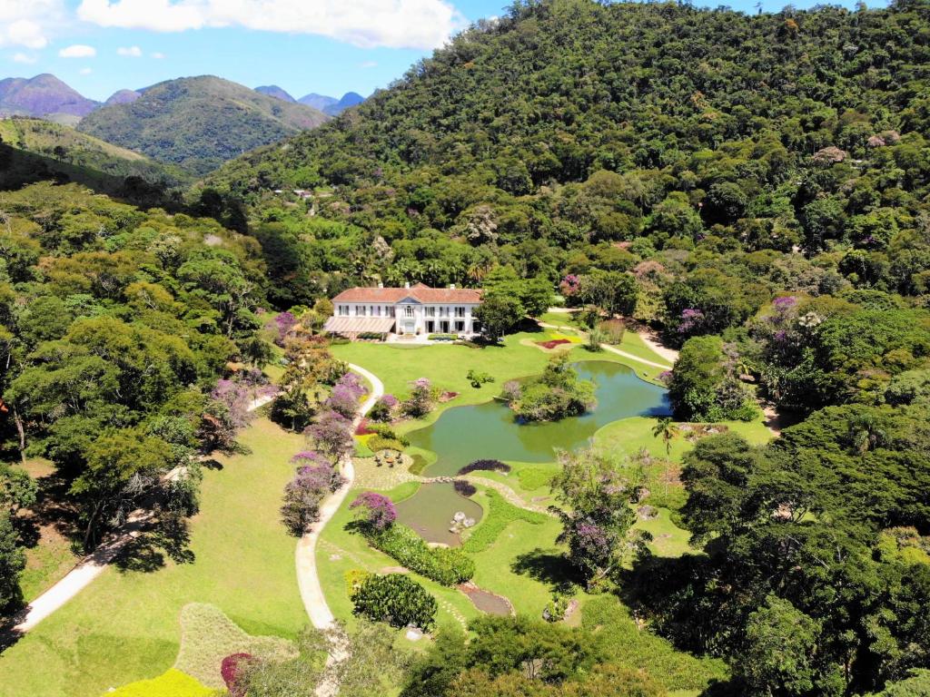 Vista aérea da propriedade Casa Marambaia Hotel, com uma construção estilo colonial ao centro, cercada por montanhas e árvores, com um extenso lago do lado direito, para representar hotéis em Petrópolis
