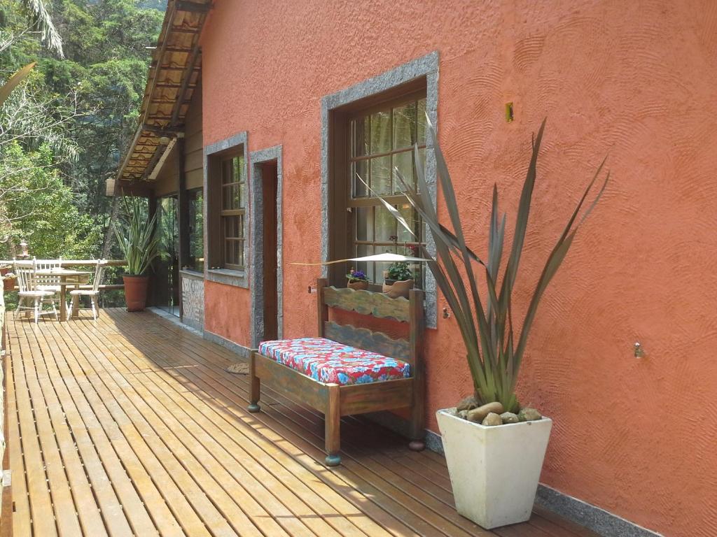 Chalé na Casa no Céu com uma varanda com deck de madeira, um banco com estofado, dois vasos de plantas, uma mesinha com duas cadeiras, com vista para as montanhas