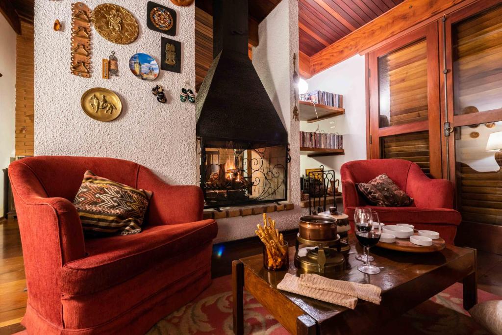 Sala da Casa Xamego Alto Padrão com uma lareira, duas poltronas vermelhas, muitos itens de decoração rústicos, uma mesa de centro de madeira com taças e alguns itens de comer