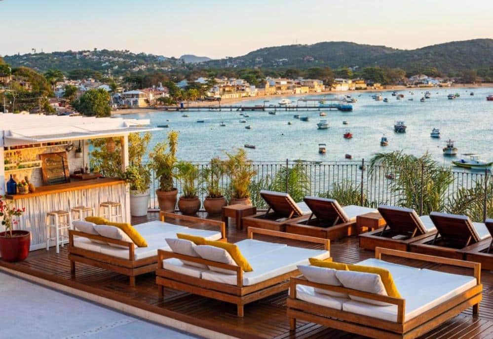 Espreguiçadeiras brancas com base de madeira em um deck com bar virado para o mar nas Casas Brancas Boutique Hotel & Spa, para representar resorts em Búzios