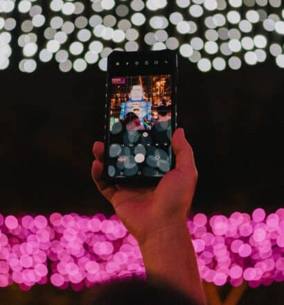 Uma mão segurando o celular em Hing Fat Street, Hong Kong para tirar foto durante a noite com várias luzes. Representa chip celular Hong Kong.