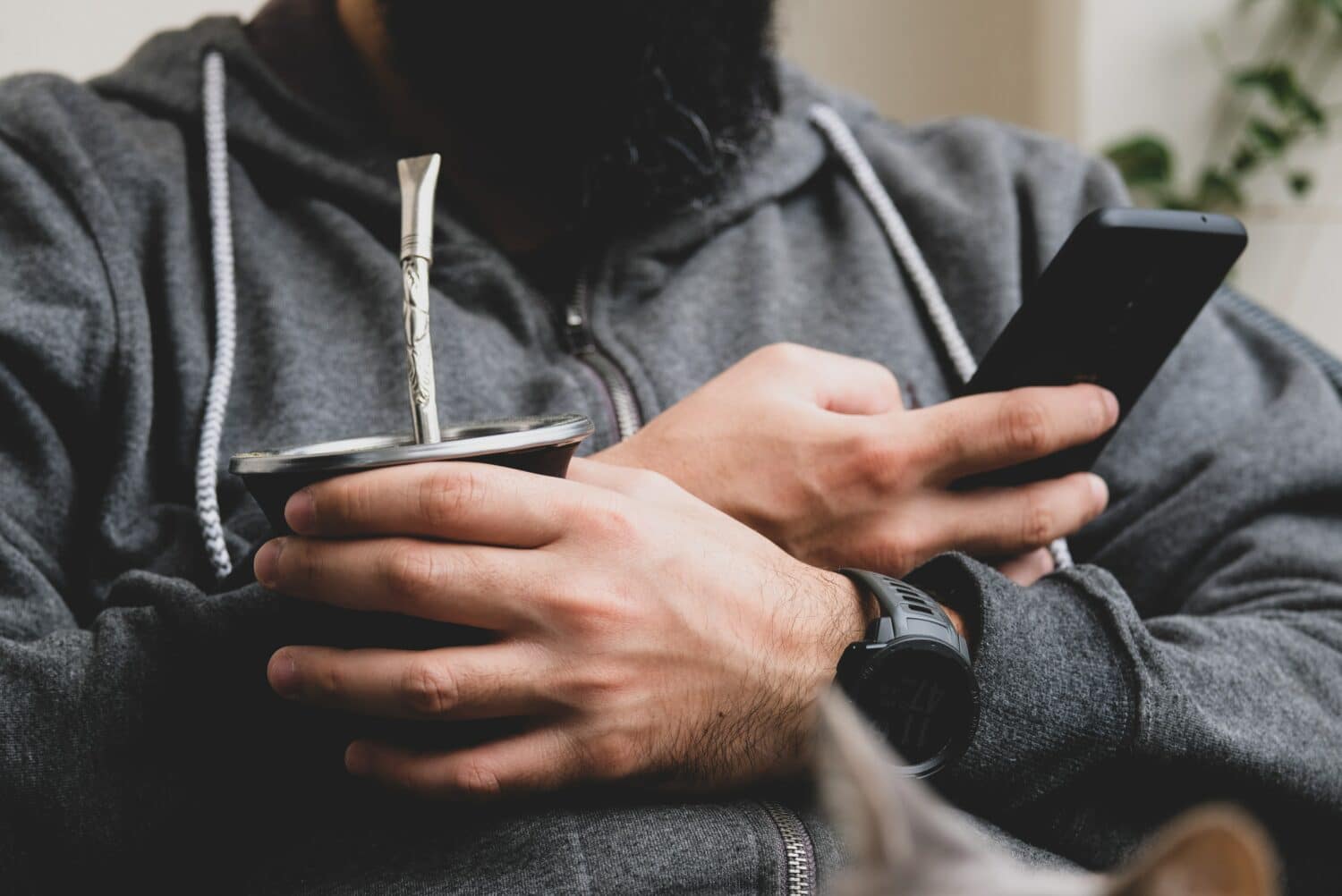 Homem de barba segurando um chimarraão na mão esquerdo e mexendo no celular com a mão direita. Representa chip celular Montevidéu