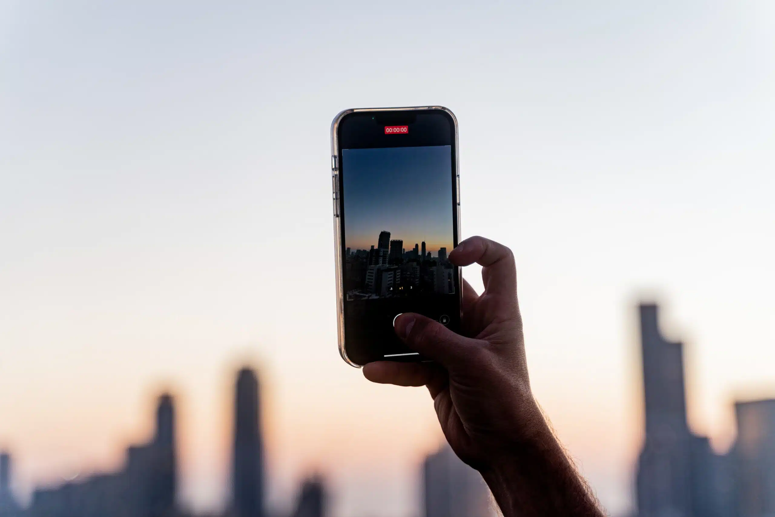Celular na mão tirando foto do por do sol em Tel Aviv, Israel. Representa chip de celular Tel Aviv
