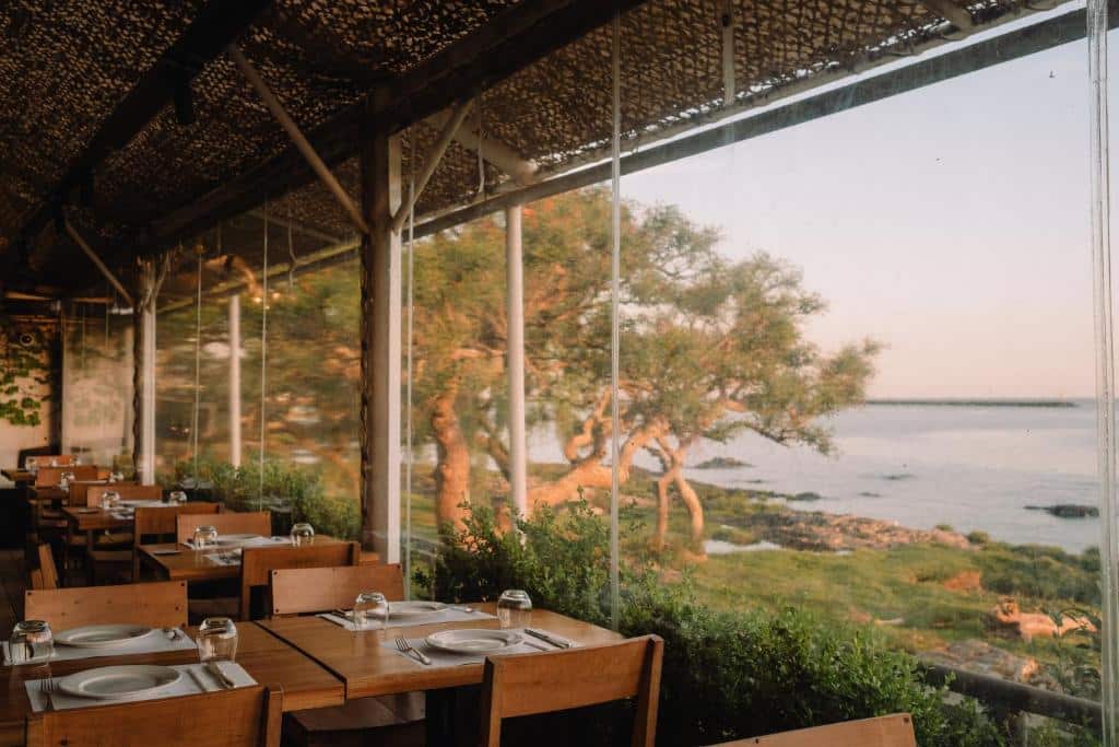 Local para refeições envidraçado do Charco Hotel com vista para uma área com árvores e o mar