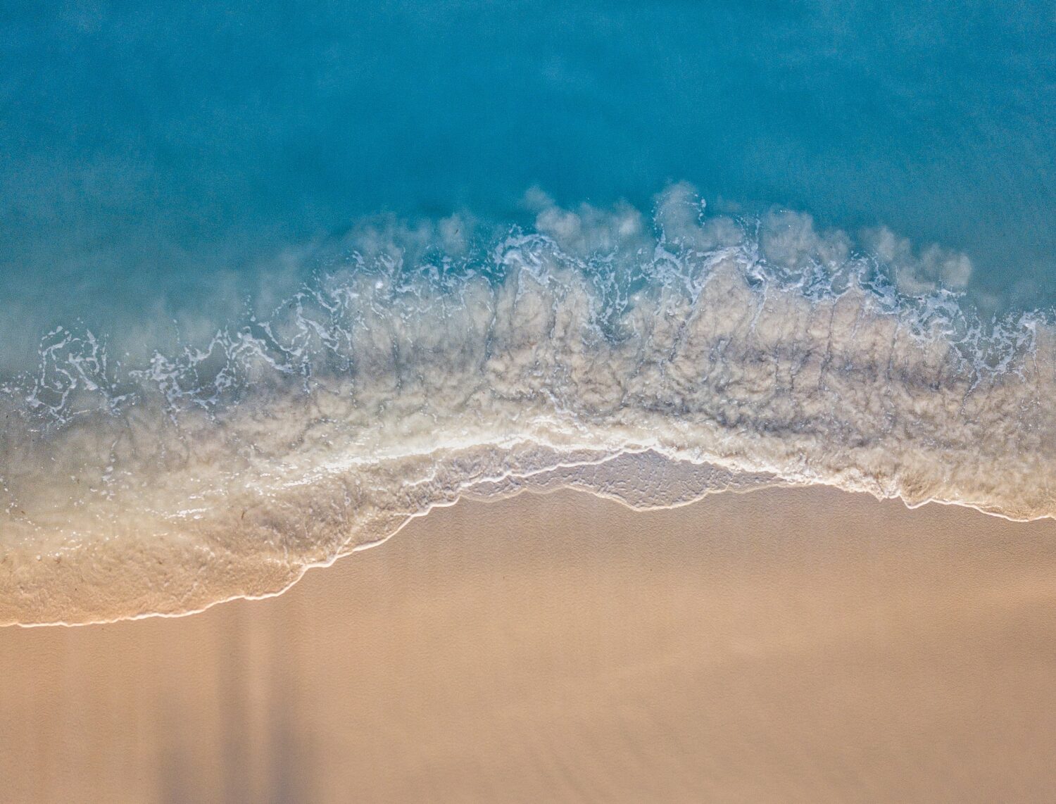 Mar azul turquesa, ondas quebrando com espuma branca, e areia dourada em praia de Aruba, ilustrando o post de chip de celular para Aruba