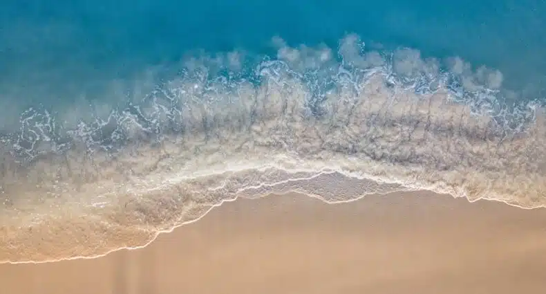 Mar azul turquesa, ondas quebrando com espuma branca, e areia dourada em praia de Aruba, ilustrando o post de chip de celular para Aruba