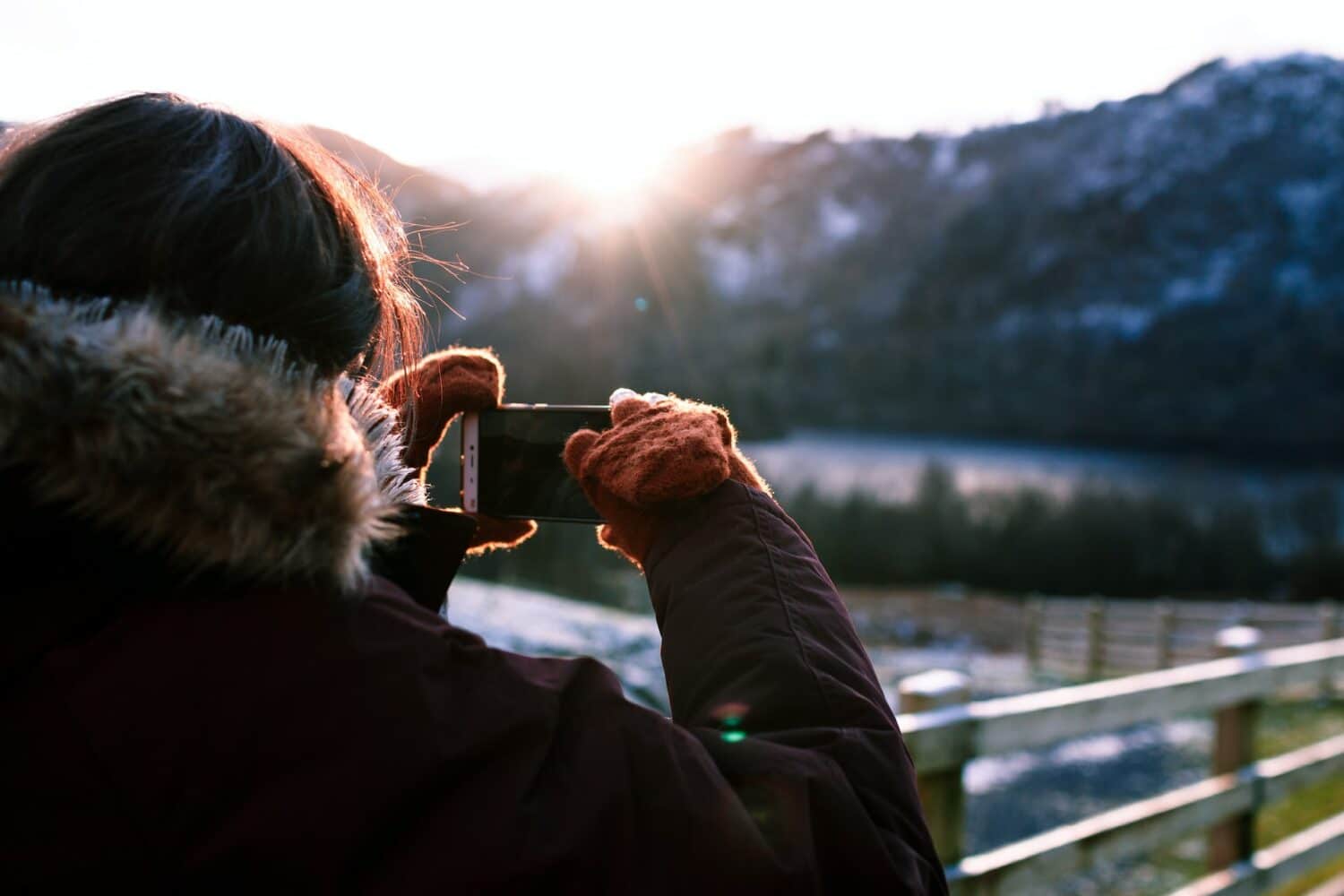 Pessoa com roupa de frio tirando foto com o celular de montanhas ao fundo durante o dia, ilustrando post chip celular Inglaterra.