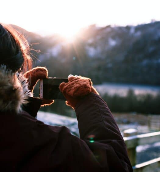 Pessoa com roupa de frio tirando foto com o celular de montanhas ao fundo durante o dia, ilustrando post chip celular Inglaterra.
