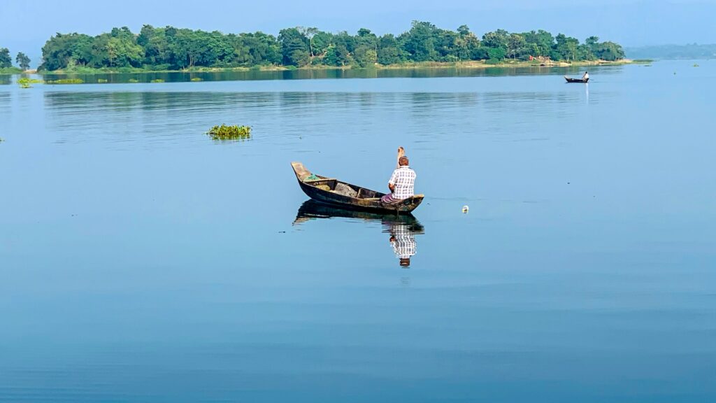 Chittagong em Bangladesh, homem navegando com uma canoa ao centro e ao fundo vasta vegetação compõe o lago com céu azul.