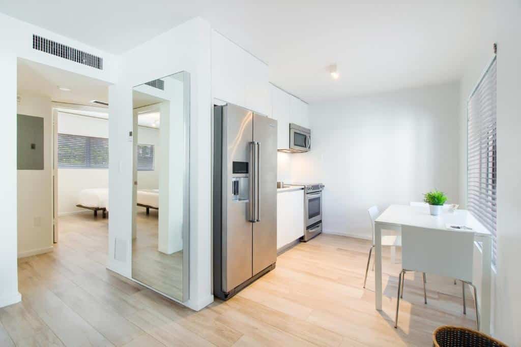 Cozinha do Beach Haus Key Biscayne Contemporary Apartments com mesa quadrada branca de três cadeiras, geladeira, pia no meio com armário e ao fundo fogão com micro-ondas em cima. Representa hotéis com cozinha em Miami.
