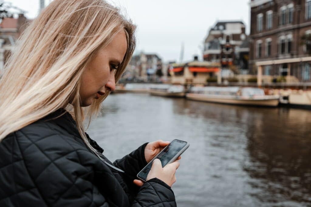 Uma moça loira mexendo em um celular perto de um dos canais de Amsterdam
