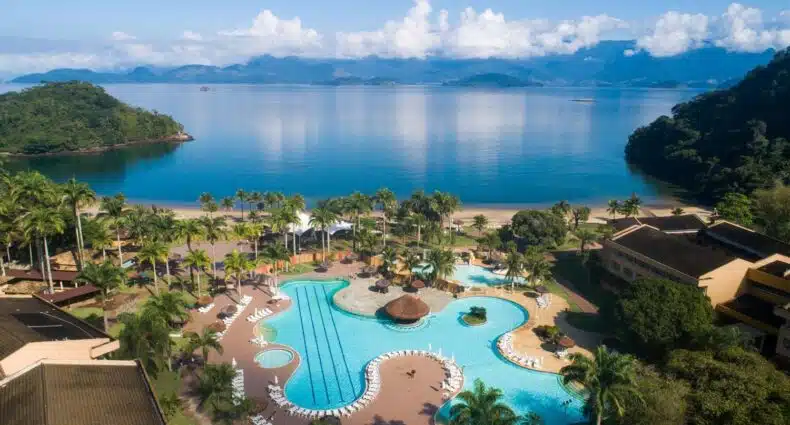 Piscina do Vila Galé Eco Resort Angra dos Reis com vista direta para o mar, com algumas árvores ao redor de toda a propriedade, e uma montanha do lado direito, para representar resorts em Angra dos Reis
