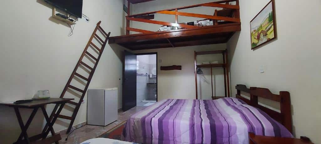 Quarto quádruplo, de 16 m², do Espaço Rural Água da Onça, com cama de casal, frigobar e uma escada encostada na parede dando acesso a um mezanino com um colchão