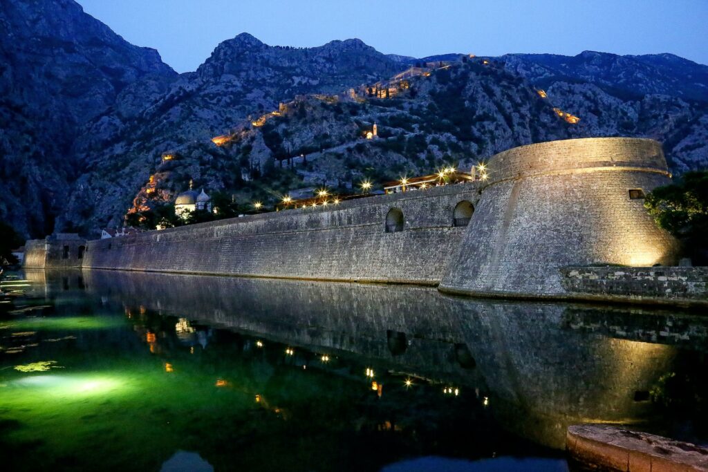 Um forte de concreto com uma ponte iluminada sob ele, cercado pelo mar e também por montanhas, para representar chip celular Montenegro