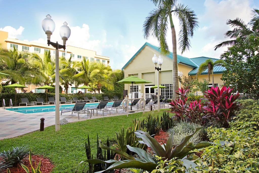 Vista do Homewood Suites by Hilton Miami – Airport West com piscina, cadeiras em volta com jardim. Representa Hotéis com cozinha em Miami.