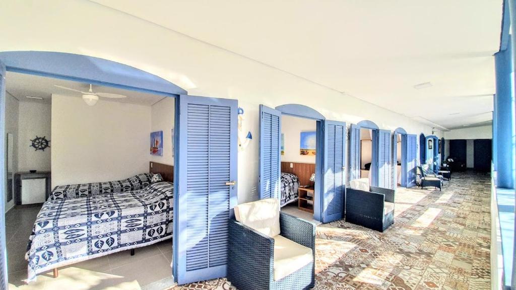 Vista da entrada do Brisa do Mar Barê Praia Hotel com vários quartos com portas azuis de madeira aberta e cadeiras de em frente dos quartos. Representa pousadas na praia de Guaecá.