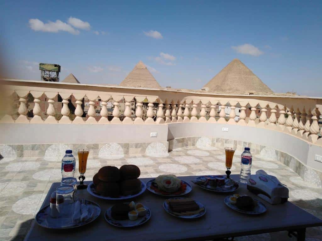 área de café do Queen Pyramids View Inn com vista das pirâmides durante o dia. Representa Hotéis no Cairo.