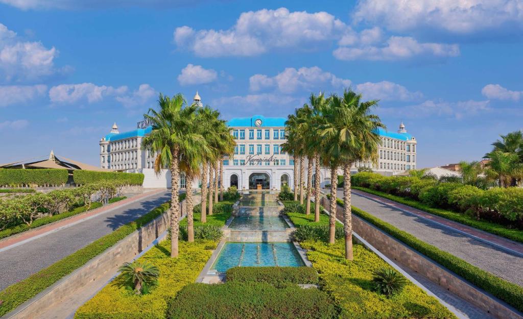 Vista da frente do Royal Maxim Palace Kempinski durante o dia com piscinas ao centro em volta de coqueiros e ao fundo o hotel. Representa Hotéis no Cairo.
