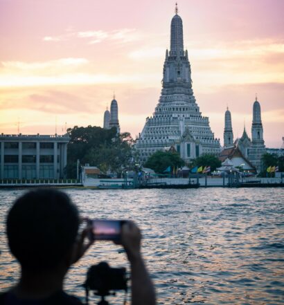 Um rapaz com o celular na horizontal fotografando um templo budista de concreto em Bangkok
