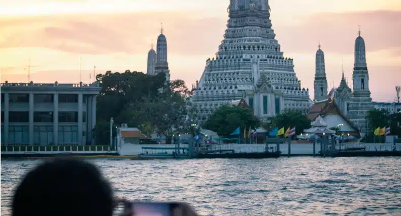 Um rapaz com o celular na horizontal fotografando um templo budista de concreto em Bangkok