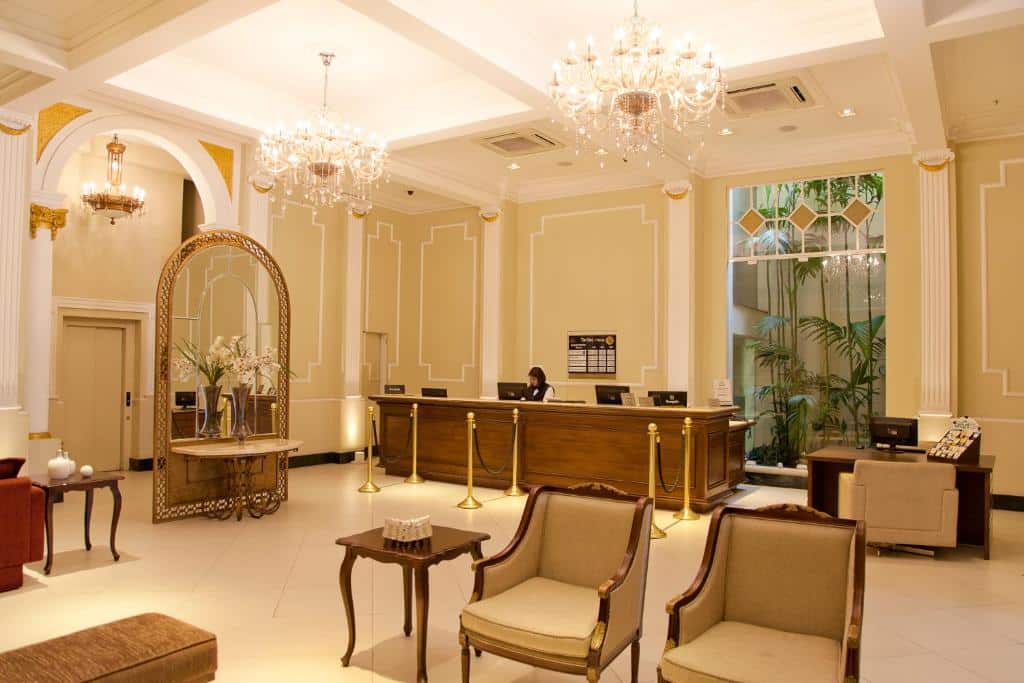 Hall do Grande Hotel Petrópolis em estilo clássico e colonial, com poltronas, lustres de cristal e um pequeno jardim de inverno
