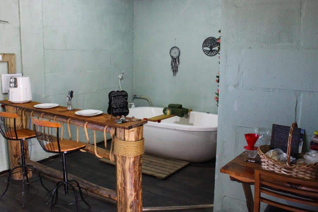 banheira de hidromassagem com algumas toalhas em cima, um enfeite de filtro dos sonhos pendurado na parede, e uma mesa estreita e rústica em frente com duas cadeiras altas e dois pratos brancos em cima