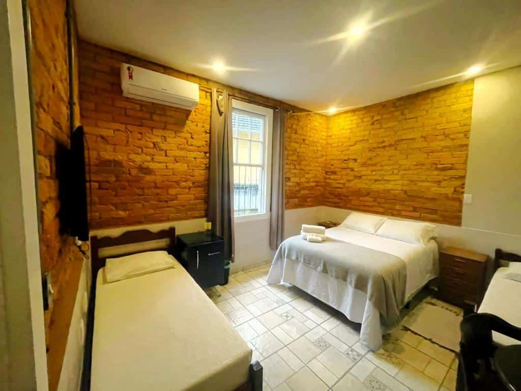 Quarto da HMG Morada & Chalet - Centro histórico com uma cama de casal, uma de solteiro, um frigobar, um ar-condicionado de parede e uma janela com cortinas