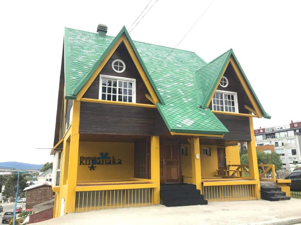 frente da Hosteria Kupanaka com uma construção em formato de chalé com telhados verdes e paredes amarelas