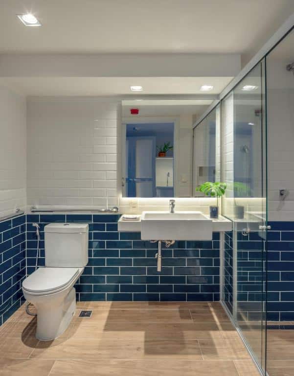 Banheiro do Hotel Aretê com uma privada com barras de apoio, uma pia sem móvel embaixo para uma cadeira de rodas encaixar e um box de vidro