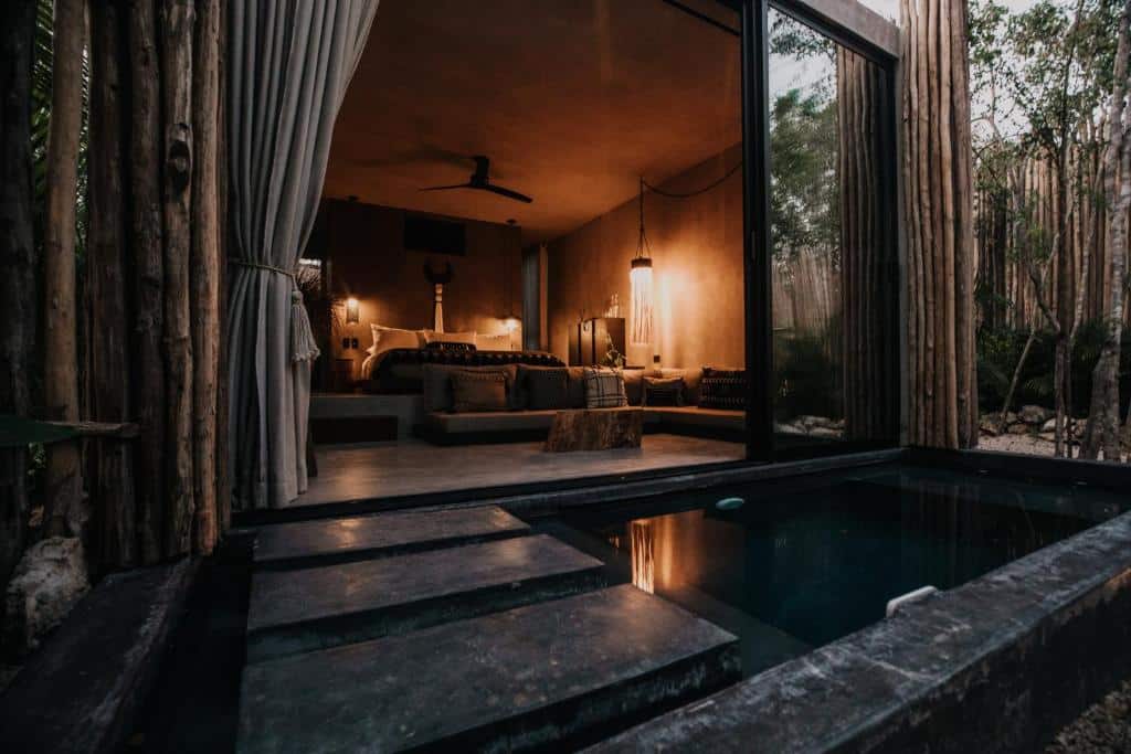 Suíte do Hotel Bardo, de 65 m², com piscina privativa na varanda, uma cama de casal com sofá no chão com almofadas em cima, ventilador no teto e uma luminária iluminando o quarto.