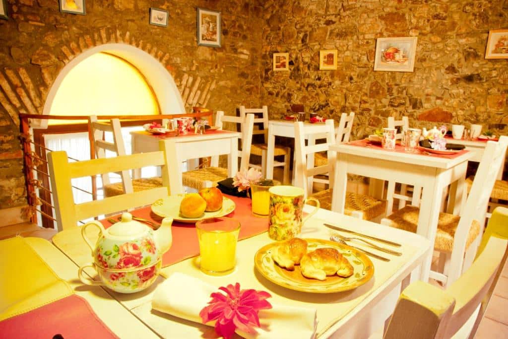 Área para refeições do Hotel La Mision com paredes de pedra, mesas e cadeiras de madeira branca e alguns quadros nas paredes